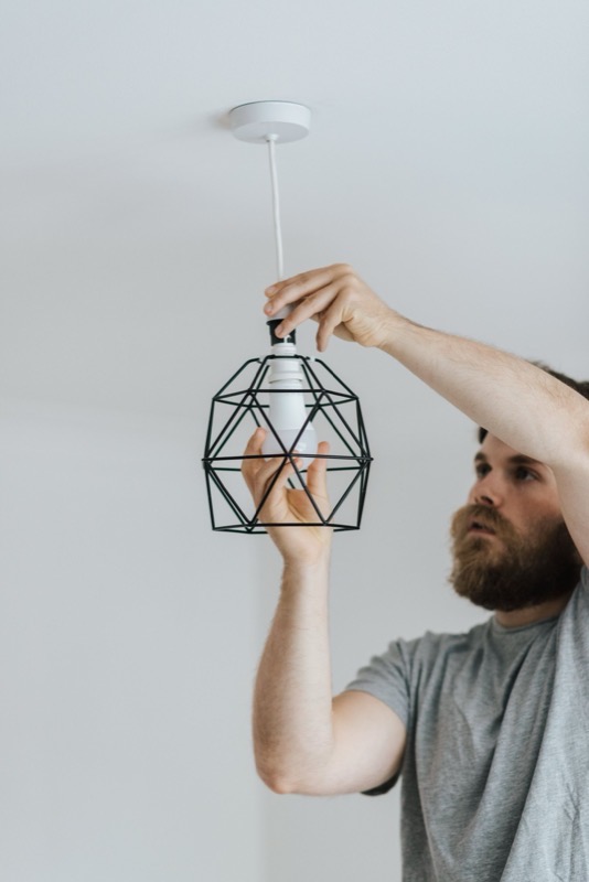 An electrician fitting a bulb into a black wire-cage pendant light