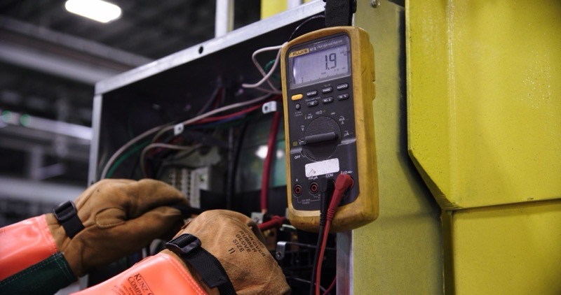 A gloved hand testing a panel with a multimeter