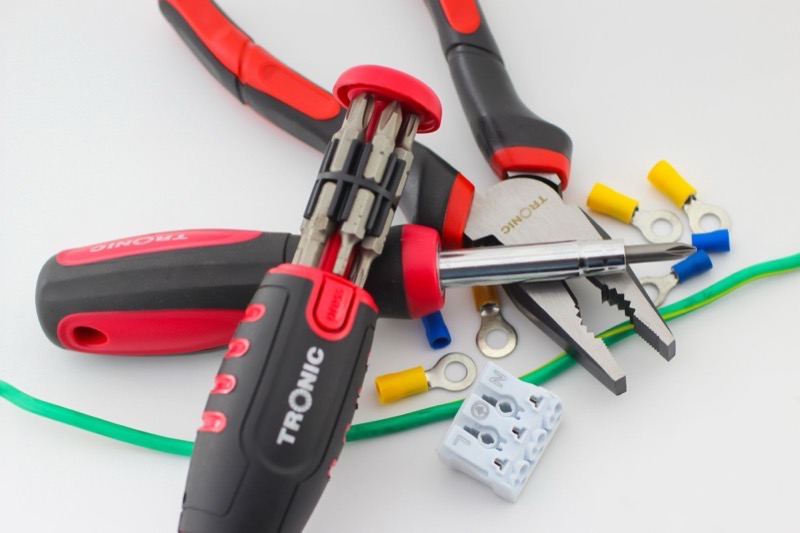 Screwdrivers, pliers, cable and crimp connectors laid out on a white surface